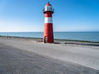 a small lighthouse on the beach near some water and cars in traffic passing by and a blue sky