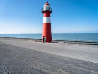 a small lighthouse on the beach near some water and cars in traffic passing by and a blue sky