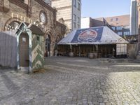 a small outdoor market with stalls in front of a brick building and a clock on the wall