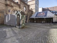 a small outdoor market with stalls in front of a brick building and a clock on the wall