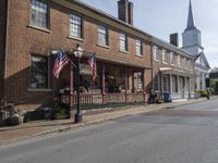 the american flag is flying over a small town street with stores in the front and people walking around the building