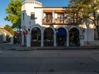 a small town store with a blue awning and tree in front of it and several flags on a balcony and a stop sign