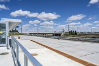 a small white bus shelter on an overpass over a bridge and a highway that passes through