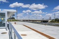 a small white bus shelter on an overpass over a bridge and a highway that passes through