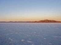 snow capped surface of an open plain with hills in the distance with yellow sky and clouds