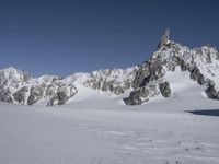 snow covered ground and a skier is going down the mountain side on skis and poles