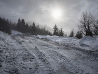 a snow covered path with snow on both sides and trees in the background with the sun