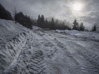 a snow covered path with snow on both sides and trees in the background with the sun