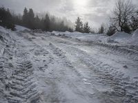 a snow covered path with snow on both sides and trees in the background with the sun