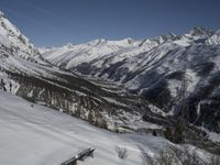 a ski slope with a wooden bench sitting next to it in the snow near mountains