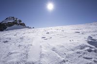 a view of a mountain covered in snow with footprints on it and sun behind it