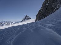 a skier standing in the snow looking off into the distance below a steep mountain peak