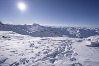 an area in the mountains covered in snow with deep blue sky and sun in the background