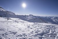 an area in the mountains covered in snow with deep blue sky and sun in the background