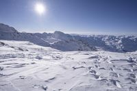 an area in the mountains covered in snow with deep blue sky and sun in the background