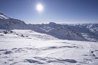 an area in the mountains covered in snow with deep blue sky and sun in the background