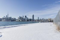 a fenced off area has snow covering the ground and is very snowy with a city in the background