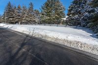 a couple of snow covered trees are near some road signs and fenced off road