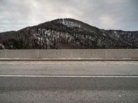 the side of a snowy road with mountains in the background and a sky background and one road has snow on it