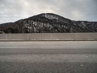 the side of a snowy road with mountains in the background and a sky background and one road has snow on it