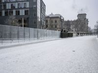 snow on the ground, building, and sidewalk next to it and fenced off with snow