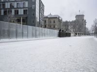 snow on the ground, building, and sidewalk next to it and fenced off with snow