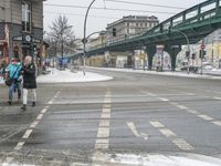 two people walking across an intersection in the snow with a pedestrian crossing over the road