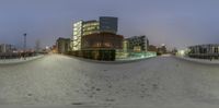 a picture of a city with snow and buildings in the background, taken on a fisheye lens