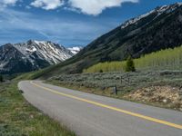 the road is paved with yellow markings and has a snowy mountain range in the background