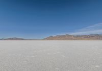 lone motorbike on a snow covered desert surface near mountains and sky line in distance