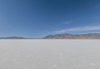 lone motorbike on a snow covered desert surface near mountains and sky line in distance