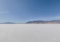 lone motorbike on a snow covered desert surface near mountains and sky line in distance