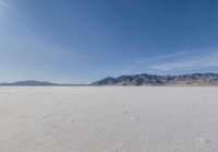 lone motorbike on a snow covered desert surface near mountains and sky line in distance