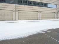 a view of a snow covered driveway next to building with large windows and shutters