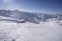 a hut is in the middle of snowy mountains with snow on it with a bright blue sky and sun over top