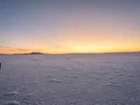 snow covered ground with a few footprints in the distance and a view of mountains at sunset