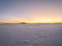 snow covered ground with a few footprints in the distance and a view of mountains at sunset