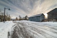 a large gray barn sitting on top of snow covered ground near trees and a road