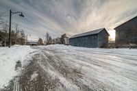 a large gray barn sitting on top of snow covered ground near trees and a road