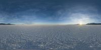 a wide view of snow covered ground with the sun in the background from high above the horizon