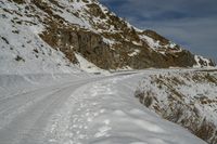 a large snow covered hill near a snowy road with some tracks of snow on it