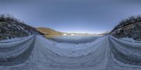 three snow covered hills overlook an alpine lake and mountains in the distance near a sandy shore