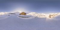 a house is sitting at the end of snow covered hills with snow capped mountains in the background