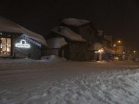 a hotel on a street covered in snow at night with light shining through windows in the corner