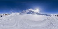 snow is piled up in an abstract shape with people skiing down it and a bright sun is shining over the snow covered mountain