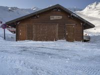 a brown barn with wooden siding covered in snow in the mountains near a road stop sign