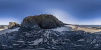 a mountain covered in snow next to the ocean with rocks near it and water and some sand