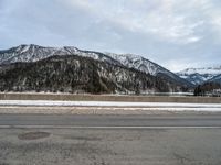 a snow - covered mountain range is seen on the edge of a highway with snow capped hills