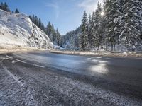 a mountain road with no vehicles or traffic is covered in snow and ice with pine trees in the background