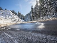 a mountain road with no vehicles or traffic is covered in snow and ice with pine trees in the background